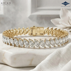 A gold tennis bracelet with marquise-cut clear stones, displayed on a white marble block with a white fabric and flower prop. The brand logos for ARIAS Lara Cutta and Sparkles are visible in the corners.