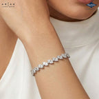 A close-up of a model's wrist wearing a Lara Dutta Arias bracelet, featuring a row of sparkling heart-shaped clear stones in a silver-toned setting. The model is wearing a white top, and the Lara Dutta brand logo is visible in the top left corner.
