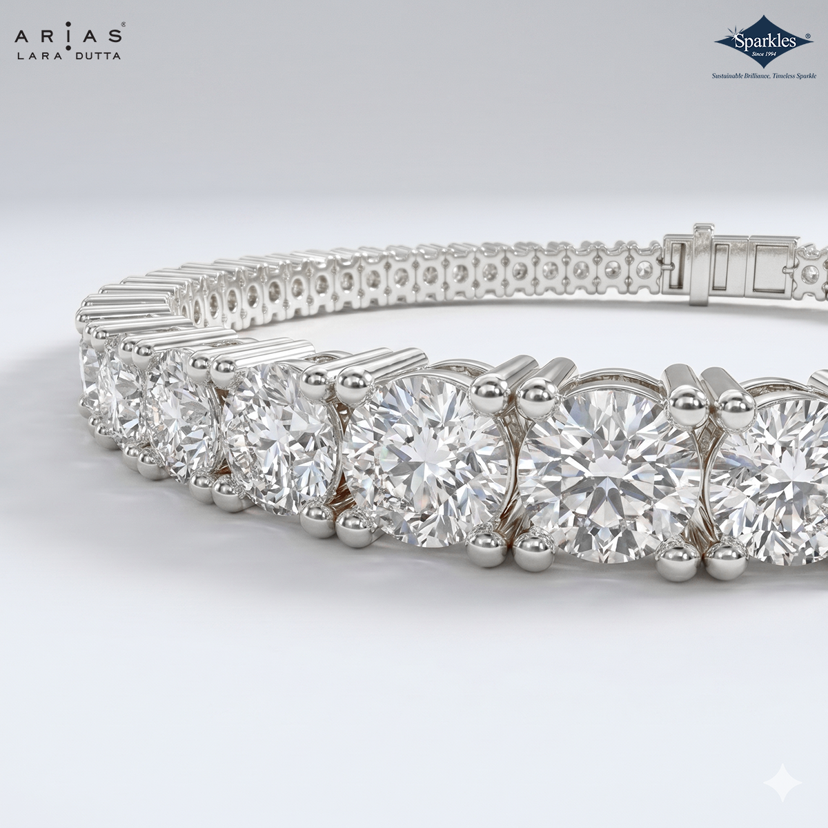 A close-up studio shot of a silver tennis bracelet with round clear gemstones, showing the detailed prong setting and clasp mechanism. The brand logos for 'Arias Lara Dutta' and 'Sparkles' are visible in the top corners.