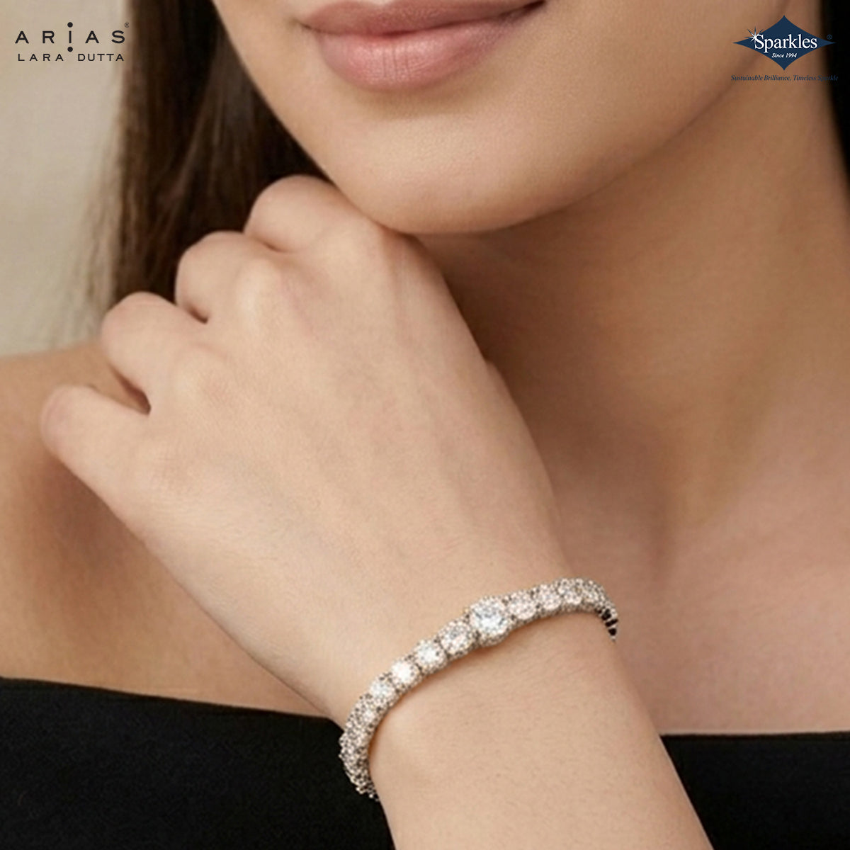 Close-up of a woman's hand wearing a diamond bracelet with Arias and Sparkles logos.