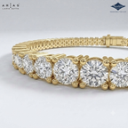 A close-up of a gold tennis bracelet featuring a row of round brilliant-cut clear gemstones, with the clasp visible in the background. The brand logos 'ARIA'S LANA GUTTA' and 'Sparkles' are visible in the top corners.