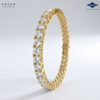 A yellow gold tennis bracelet featuring round brilliant-cut diamonds, shown on a light gray gradient background. The brand logos for 'Arias Lara Cutta' and 'Sparkle' are visible in the top corners.