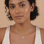 Woman wearing a silver necklace with a floral pendant against a beige background