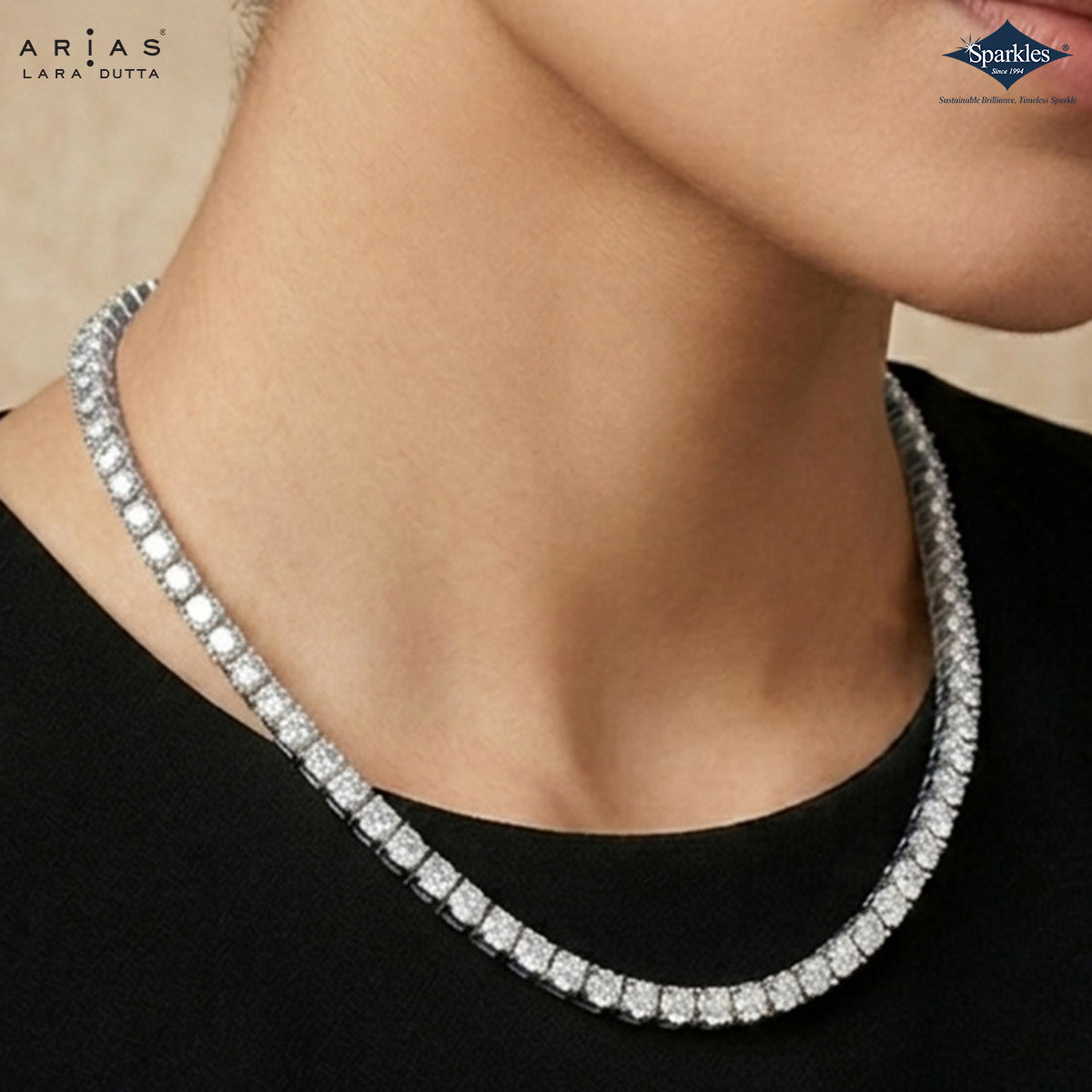 A close-up of a model's neck and lower face wearing a sparkling silver tennis necklace with clear stones. The brand logos 'ARIA'S LARA DUTTA' and 'Sparkles' are visible in the top corners.