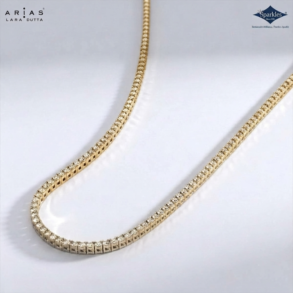 A gold tennis-style chain necklace with pavé-set clear stones, photographed on a clean white background. The Arias Lara Gutta brand logo appears in the top left, and a Sparkle watermark is visible in the top right.