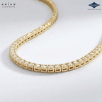 A gold tennis necklace with pavé-set clear stones, shown in a curved loop on a light gray background. The brand logos for 'Ariás Lara Gutta' and 'Sparkle' are visible in the top corners.