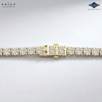 A close-up of a gold tennis bracelet with clear round-cut gemstones, showing the clasp and side links on a light gray background. The ARIAS LARA CUTTA logo is in the top-left corner, and the Sparkle Certified Gemstone logo is in the top-right.