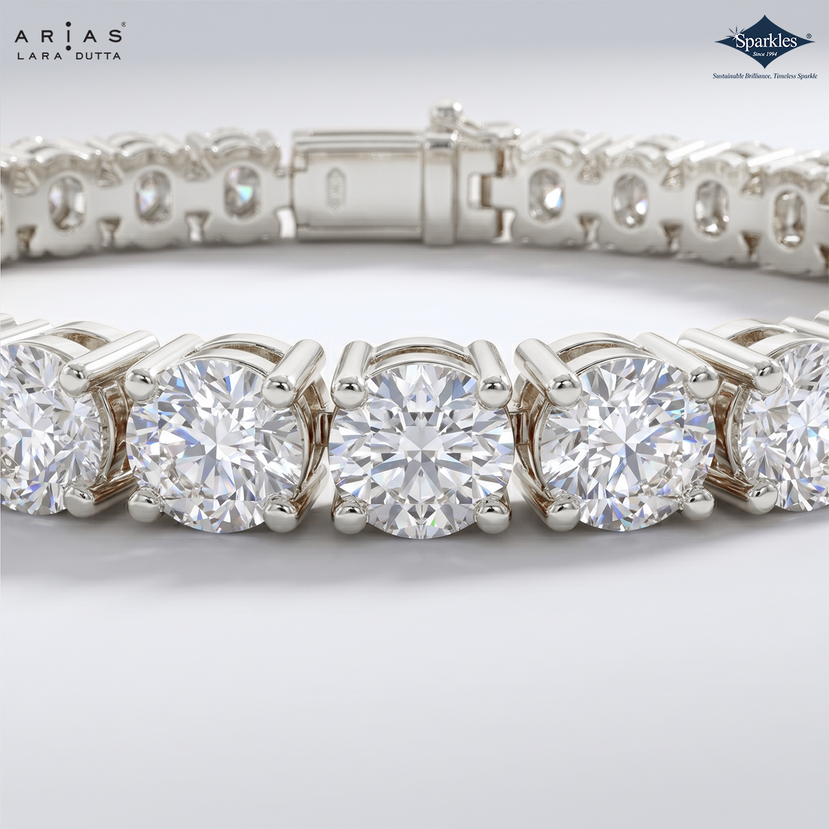 A close-up studio shot of a silver tennis bracelet featuring round brilliant-cut diamonds. The brand logos for 'Ariás Lara Dutta' and 'Sparkles' are visible in the top corners.