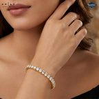 A gold tennis bracelet with clear round-cut gemstones worn on a woman's wrist, shown in a close-up lifestyle shot. The brand logos 'Arias Lara Ditta' and 'Sparkles' are visible in the corners.