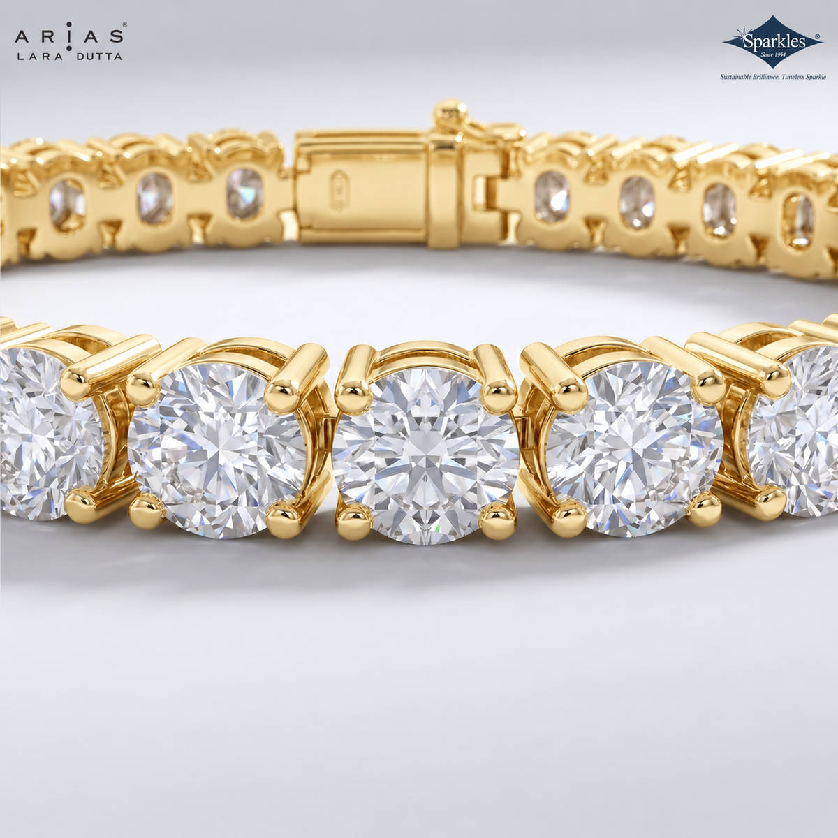 A close-up studio shot of a gold tennis bracelet with round clear gemstones, showing the clasp and part of the link pattern. The brand names ARIAS LARA DUTTA and Sparkles are visible in the top corners.