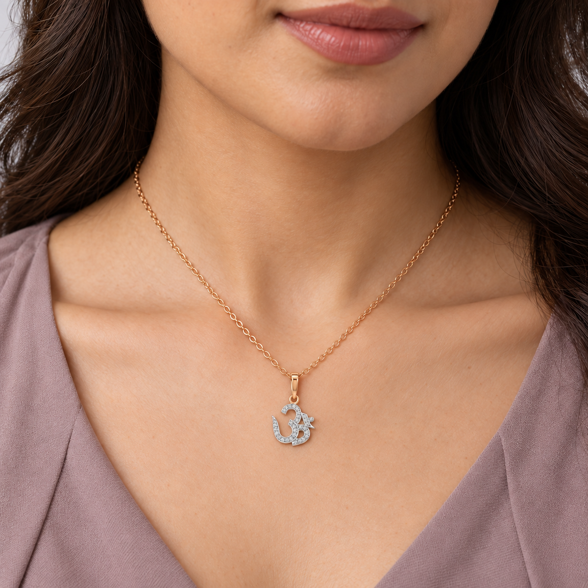 A close-up of a woman wearing a delicate rose gold chain necklace with an Om symbol pendant adorned with small clear stones, paired with a mauve top.