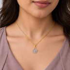 A close-up of a woman wearing a delicate gold chain necklace with an Om symbol pendant adorned with small clear stones, shown against her collarbone and chest.