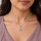 A close-up of a woman wearing a silver chain necklace with a silver Om pendant adorned with small clear stones, shown against her collarbone and chest.