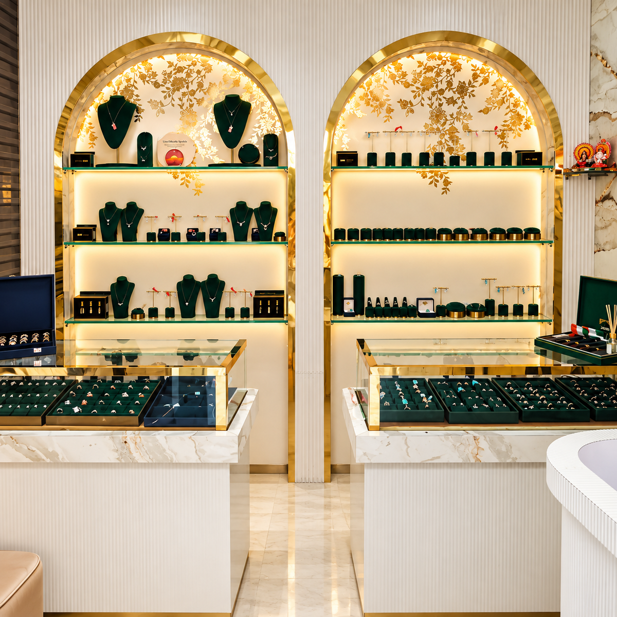 A luxury jewelry store interior with two tall arched display alcoves framed in gold, showcasing illuminated white walls, shelves, and glass cases filled with jewelry. The foreground features marble-topped counters with glass fronts and dark display trays.
