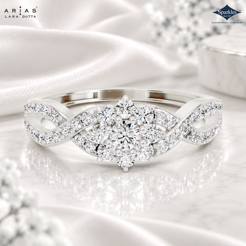 A silver-tone diamond ring with a central round diamond and surrounding diamond clusters on an infinity-shaped band, displayed on white satin fabric with a marble surface. ARIA DUTTA branding is visible in the top left, and Sparkles by Lara Dutta appears in the top right.