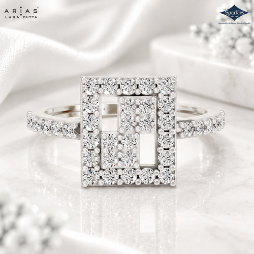 A silver-tone geometric square ring with multiple round-cut diamonds, presented on a white marble surface with a satin fabric backdrop. The brand logos for 'Arias Lara Dutta' and 'Spackle' are visible in the top corners.