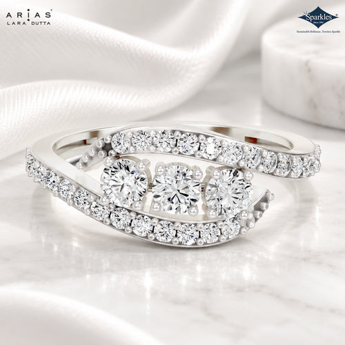 A silver-tone Lara Dutta Arias ring with three round-cut center diamonds and rows of pavé diamonds, displayed on a white marble surface with draped white satin fabric.
