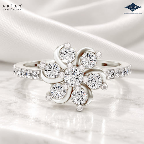 A silver-tone floral ring with clear round-cut gemstones, shown on a soft white satin fabric background. The brand logos 'ARIAS LARA DUTTA' and 'Sparkle' are visible in the top corners.