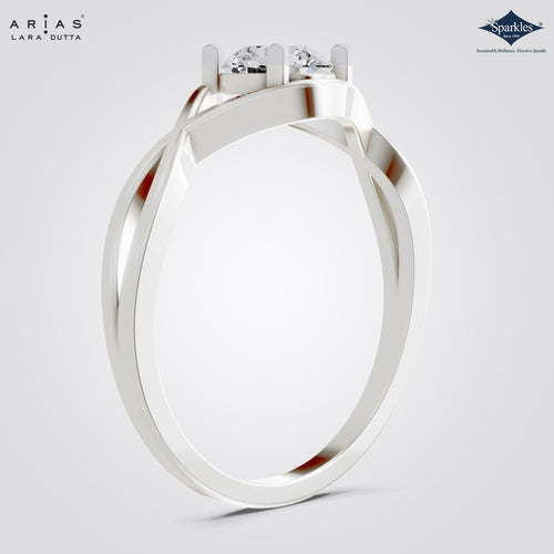A silver-toned ring with a twisted wrap-around band and a three-prong setting holding clear gemstones, shown on a light gray background. The brand names 'Ariás Lara Dutta' and 'Sparkle' are visible in the corners.