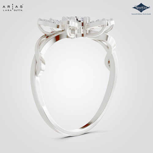 A silver-colored diamond ring by Arias Lara Dutta, featuring a bow-like top setting with small clear stones and a twisted band, shown on a light gray background.
