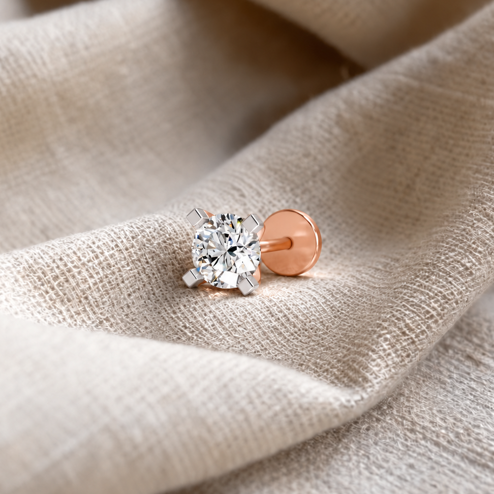 A single solitaire stud earring with a round brilliant-cut clear gemstone in a silver-toned prong setting and a rose gold post and backing, resting on a textured beige linen fabric.