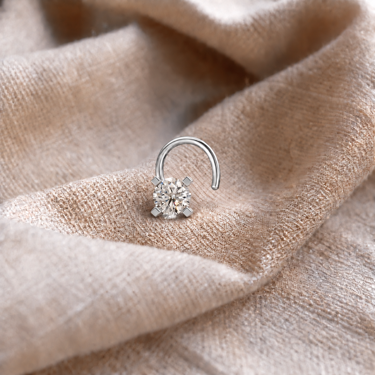 A silver-toned curved hoop earring with a single round clear gemstone, resting on draped beige fabric.