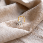 A gold hoop nose ring with a single round-cut clear gemstone in a silver-toned setting, resting on draped beige linen fabric.