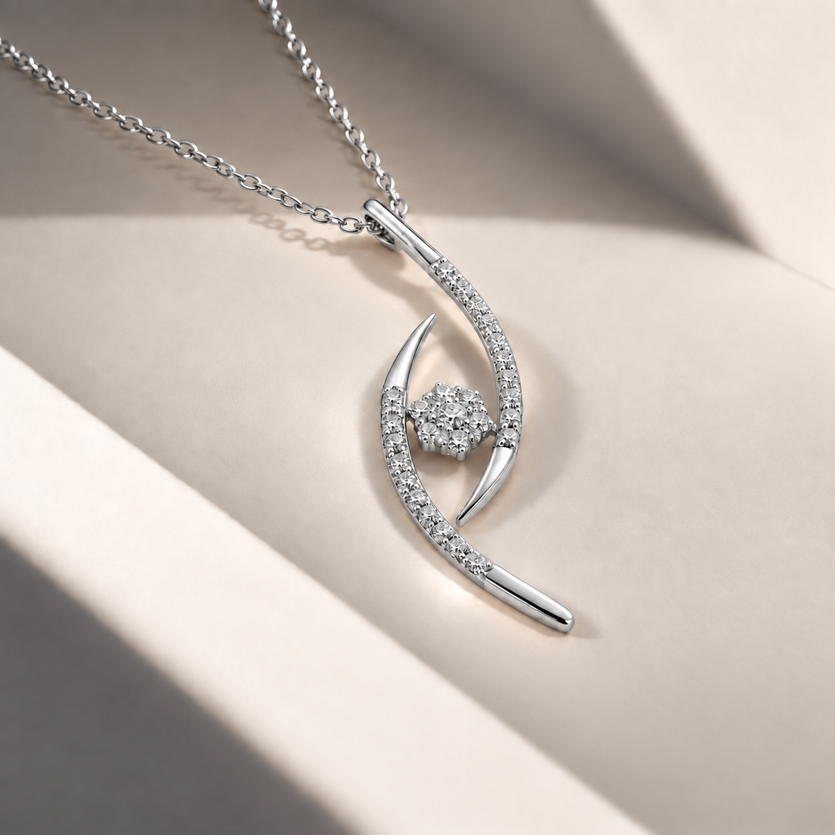 A silver pendant necklace with a curved, openwork design set with small clear stones and a central round stone cluster, displayed on a beige surface with soft shadows.