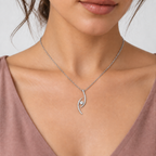 A close-up of a model wearing a delicate silver chain necklace with a curved, wave-like pendant set with small clear stones and a central clear gemstone.