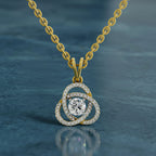 A gold chain necklace with a pendant featuring a central round clear gemstone surrounded by three interlocking curved halo settings paved with small clear stones, shown on a dark blue textured background.
