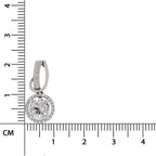 A silver-toned huggie hoop earring with a round halo pendant set with clear stones, shown next to a black ruler with centimeter markings to indicate scale.