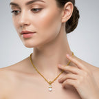 Woman wearing a gold necklace with a clear pendant on a neutral background