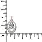 A silver-toned oval pendant with a central round clear gemstone and small accent stones, shown next to a centimeter ruler for scale on a white background.