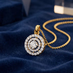 A gold pendant necklace with a circular, multi-halo diamond design, resting on a textured dark blue velvet surface.
