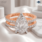 A rose gold ring set featuring a pear-cut diamond center stone and pavé-set diamonds on the bands, displayed on a soft white fabric surface with a marble prop. The brands 'Ariás Lara Dutta' and 'Sparksle' are visible in the top corners.
