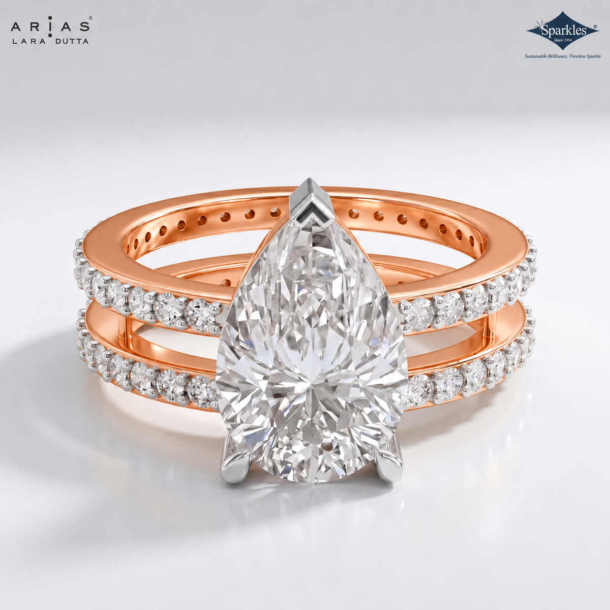 A double-band rose gold ring set featuring a large pear-cut diamond center stone and smaller diamonds along the bands, shown on a clean white background with ARIAS LANA DUTTA branding.