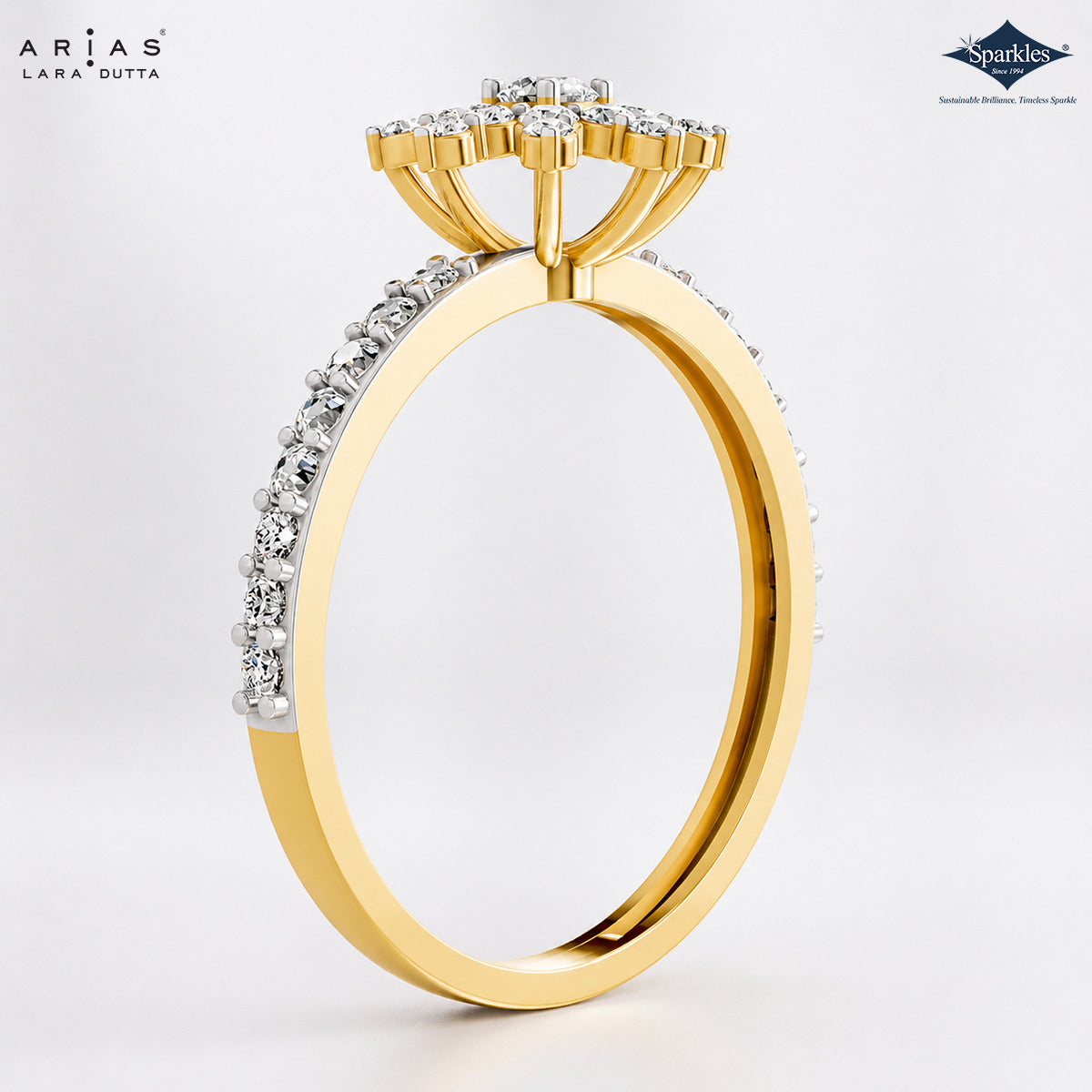 A yellow gold ring with a diamond cluster crown and a pavé band, shown from a side angle on a light gray background. The brand logos 'Ariás Lara Dutta' and 'Sparkle' are visible in the top corners.