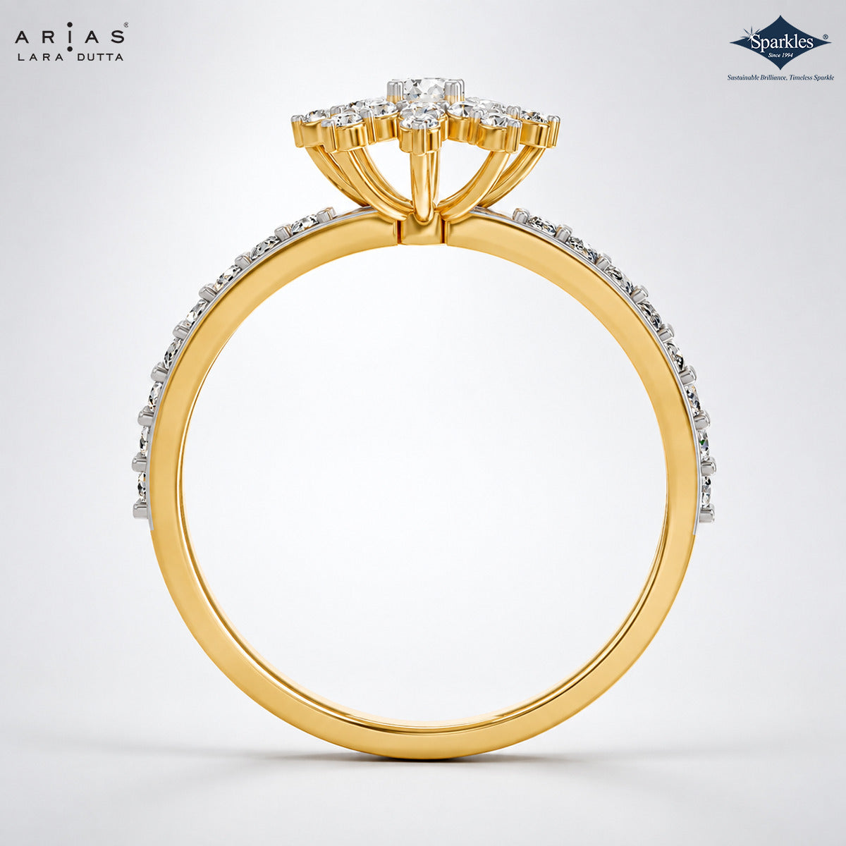 A yellow gold ring with a diamond cluster crown and a pavé-set diamond band, shown from the side on a light gray background. The brand logos 'Ariás Lara Dutta' and 'Sparkle' are visible in the top corners.