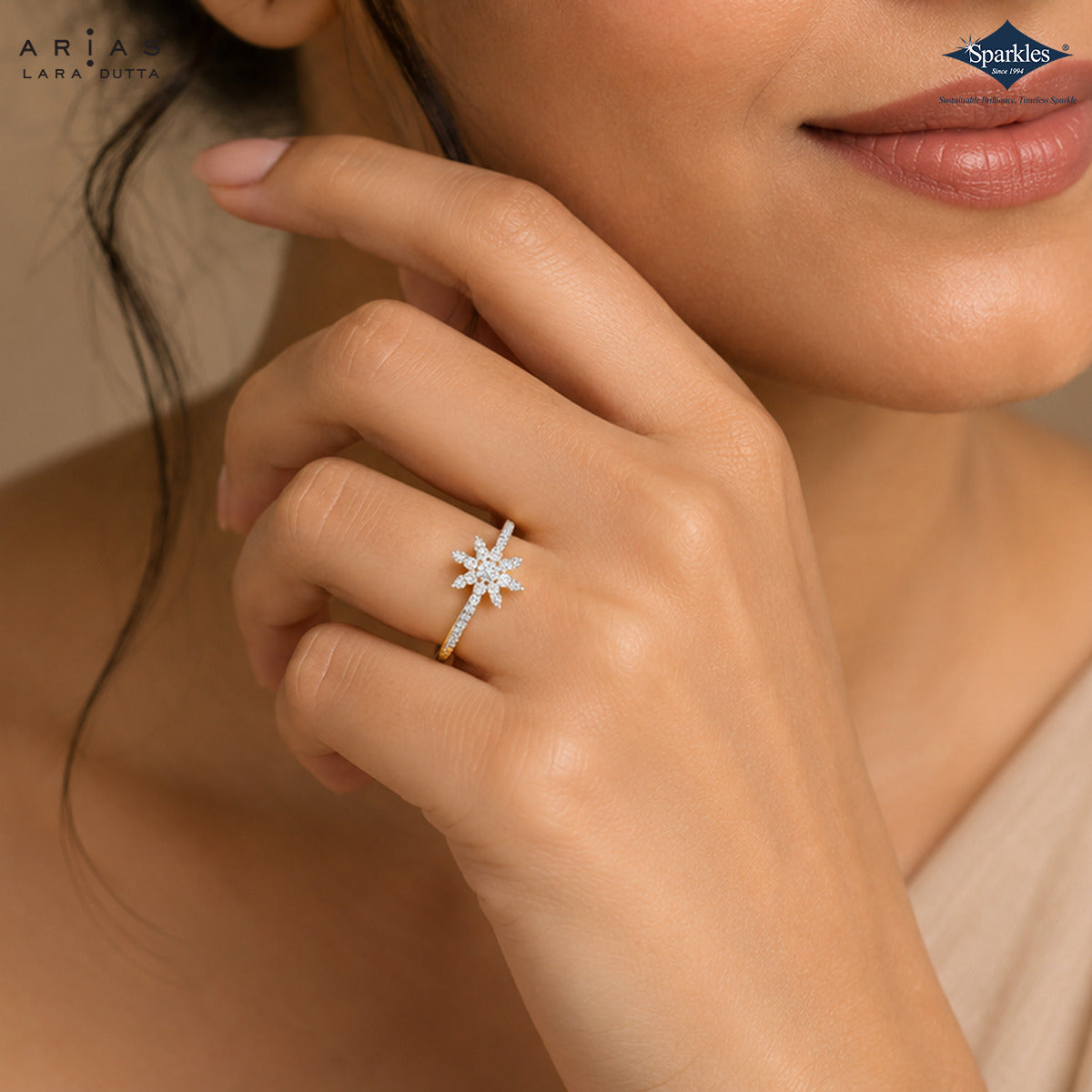 A close-up lifestyle shot of a model wearing a silver-toned ring with a starburst cluster of clear gemstones. The brand logos for 'ARIA LARA PINTA' and 'Sparksle' are visible in the top corners.