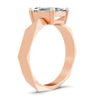 A rose gold ring with a faceted, geometric band and a clear rectangular gemstone in a four-prong setting, shown on a clean white background.